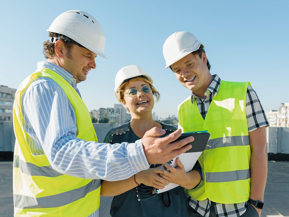 Three people in safety vests and hard hats looking at a tablet.