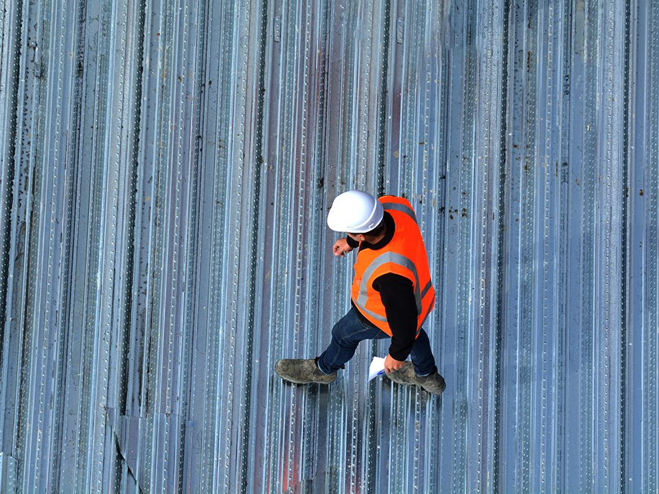 A man in an orange vest and hard hat climbing up the side of a building.